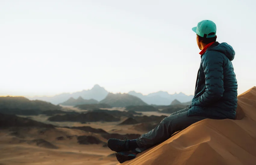 Hombre sentado sobre una duna mirando hacia el horizonte